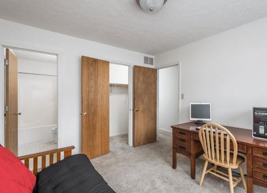 A room with a bed, desk, and two doors.