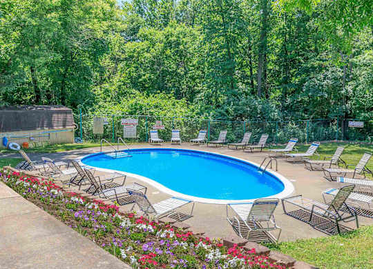 A pool surrounded by lawn chairs and flowers.