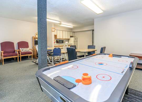 A shiny air hockey table is in the middle of a room with chairs and a kitchen in the background.