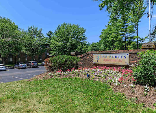 The Bluffs Apartments sign is on a brick wall with a parking lot in the background.