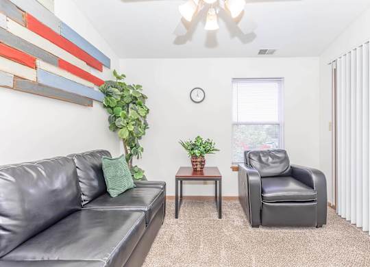 A living room with a grey couch, a black leather chair, and a wooden table with a plant on it.