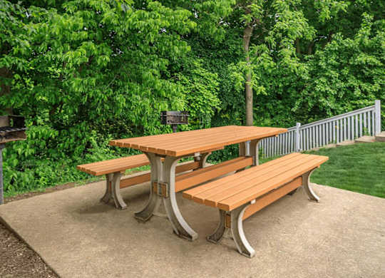 A wooden picnic table with two benches is set on a concrete surface.