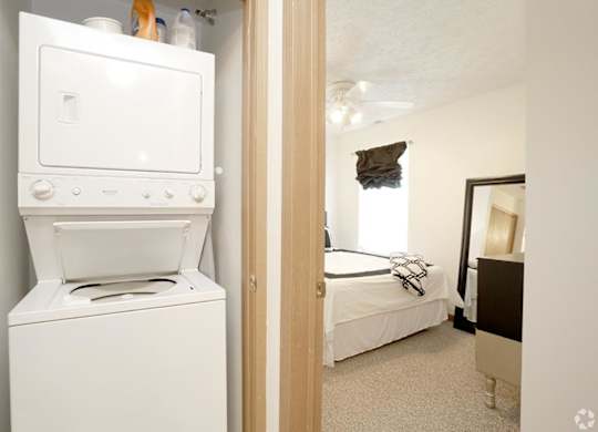 A white oven and dryer are in a small room with a bed in the background.
