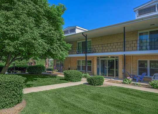 A building with a yellow brick exterior and a balcony overlooking a green lawn.