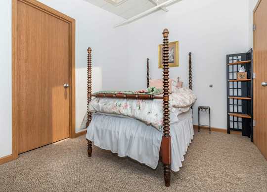 A bed with a wooden frame and four posts is in a room with a carpeted floor.