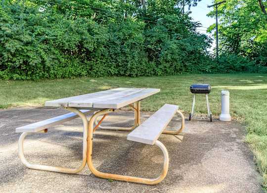 A picnic table with a grill and a cooler on a concrete surface.