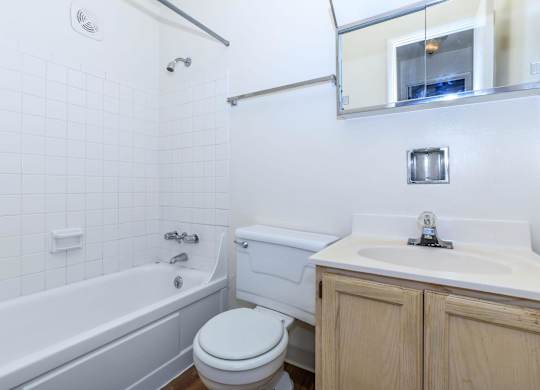 A white tiled bathroom with a white toilet, white sink, and white bathtub.