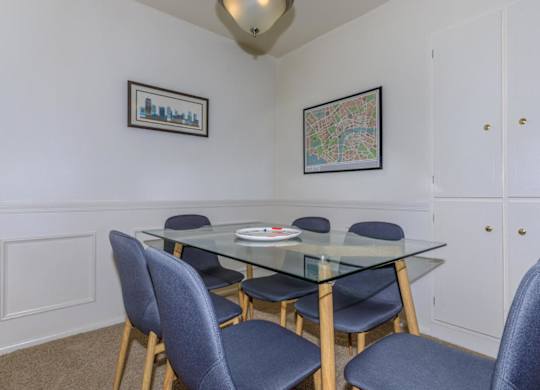 A glass dining table with four chairs and two pictures on the wall.