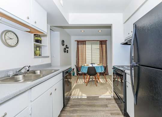 A kitchen with a black refrigerator and a dining table with chairs.