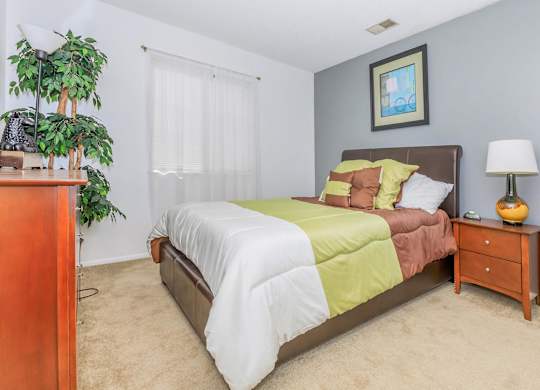 A bedroom with a bed, nightstand, and a potted plant.