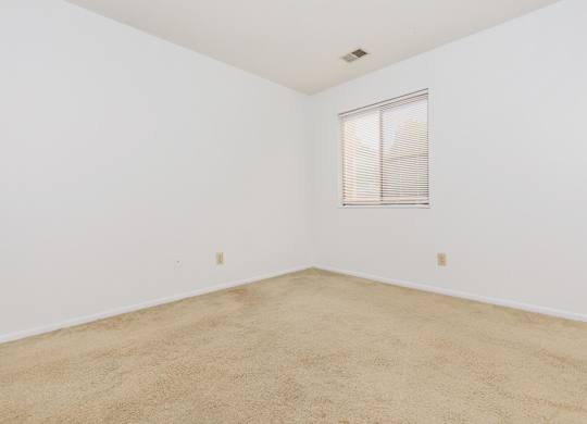 A room with a carpeted floor and a window with blinds.