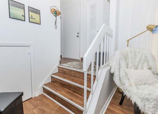 A white chair with a fluffy white blanket is in front of a staircase.