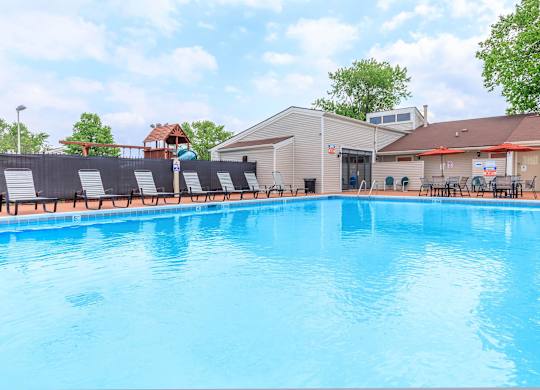 A large blue swimming pool with sun loungers and a building in the background.