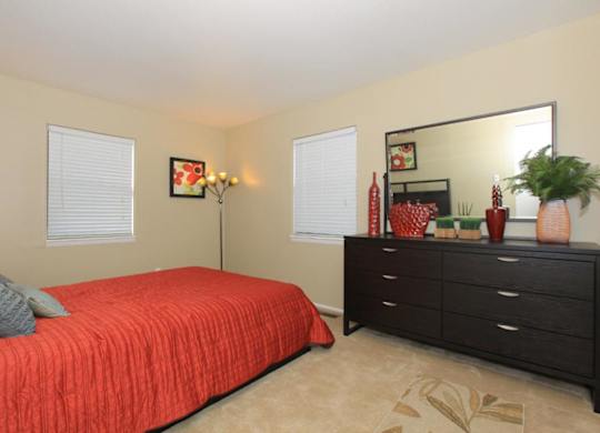 A bedroom with a red bedspread and a black dresser.