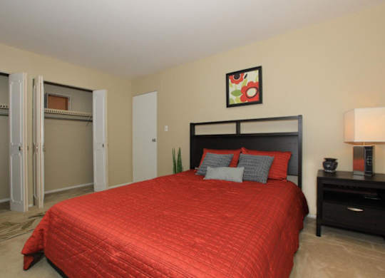 A bedroom with a red bedspread and a black headboard.
