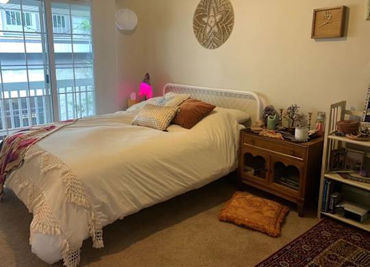 A bedroom with a white bed and a window with a view of a balcony.
