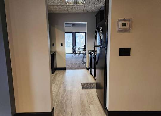 A hallway with a black fridge and a door leading to a balcony.