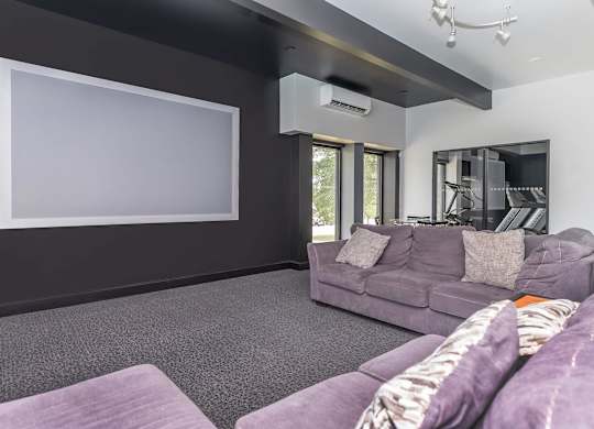 A living room with a grey couch and a large empty white screen on the wall.