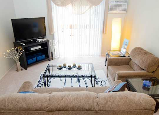 A living room with a brown couch, a glass coffee table, and a television.