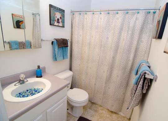 A bathroom with a white toilet, a sink with blue beads, and a shower curtain.