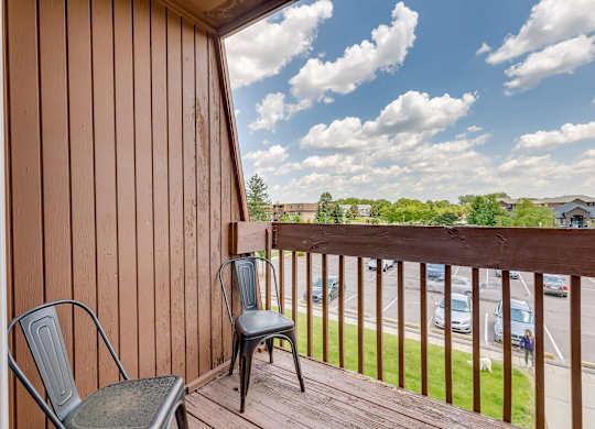 A chair sits on a wooden deck overlooking a parking lot.