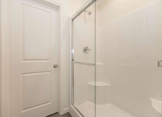 A white door is open to a glass shower stall.