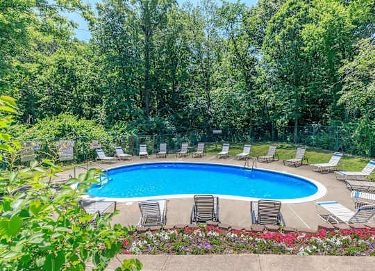 A pool surrounded by chairs and trees.