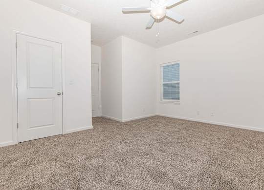 A room with a carpeted floor and a ceiling fan.