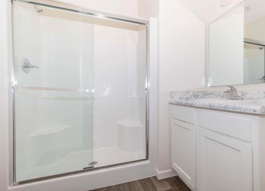 A white bathroom with a glass shower door and a marble counter.