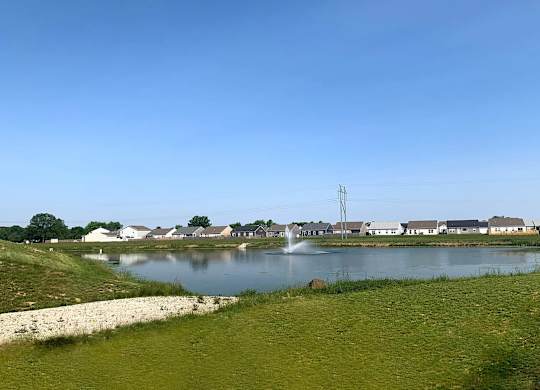 A body of water surrounded by grass and houses in the distance.