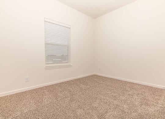 A room with a carpeted floor and a window with blinds.