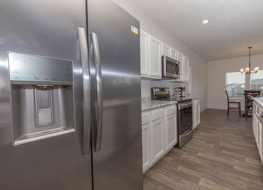 A modern kitchen with a stainless steel refrigerator and wooden flooring.