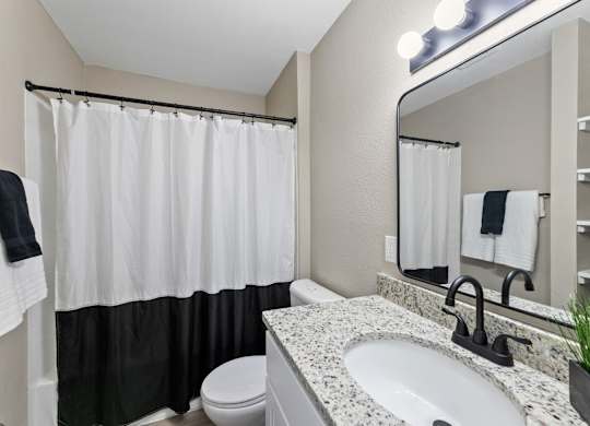 A bathroom with a white sink, toilet, and a shower with a black and white curtain.