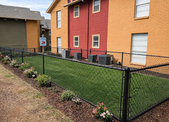 A black fence surrounds a green lawn in front of a red and orange building.