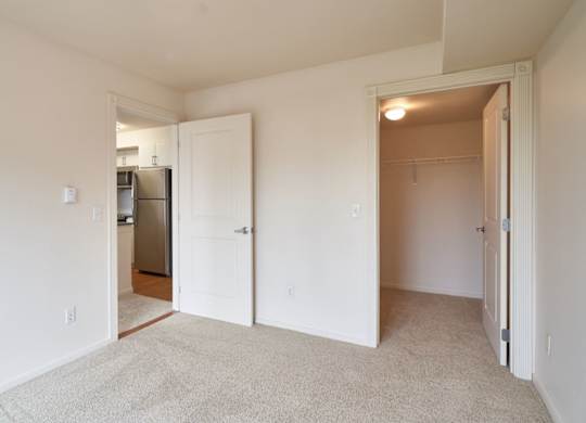 A white room with a carpeted floor and a refrigerator in the kitchen area.