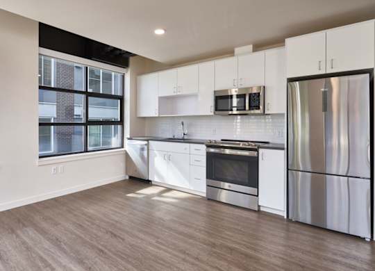 A modern kitchen with stainless steel appliances and wooden flooring.