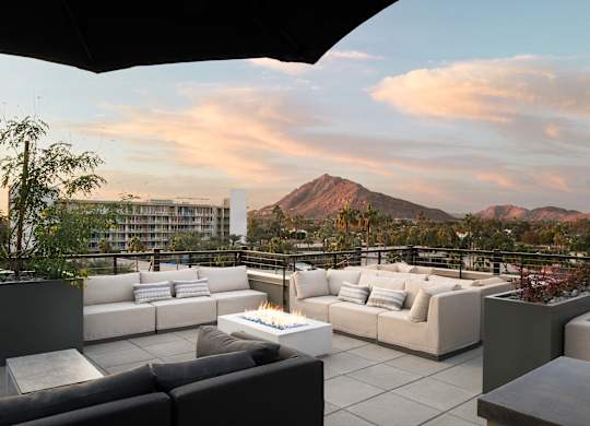 A patio with a fire pit and couches overlooks a mountain.