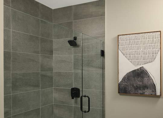 A modern bathroom with a glass shower stall and a framed artwork on the wall.