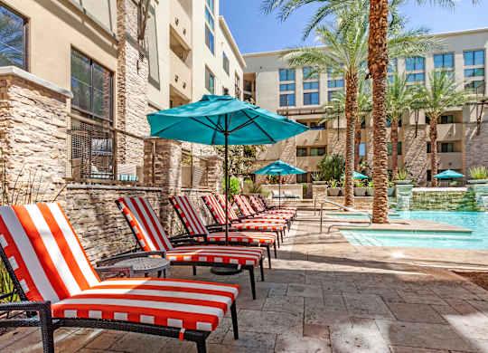 A pool area with red and white striped chairs and a blue umbrella.