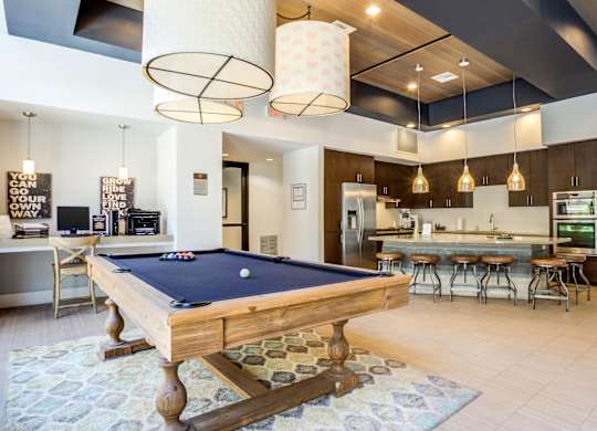 A pool table is in the middle of a room with a kitchen in the background.