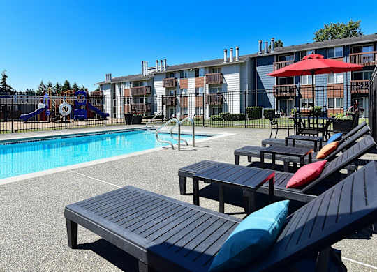 A pool area with black lounge chairs and a playground in the background. at Brookstone, SeaTac, WA, 98198
