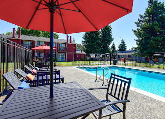 A pool area with a red umbrella and a table and chairs. at Brookstone, SeaTac, Washington