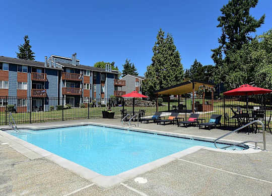 A swimming pool surrounded by a black fence with red umbrellas and chairs. at Brookstone, Washington