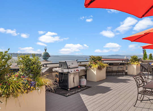 A patio with red umbrellas and a grill overlooking the water.