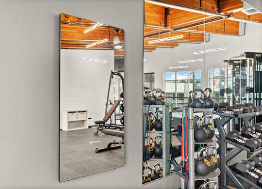 A gym with a mirror reflecting a workout area.