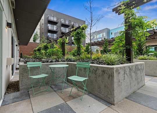 a patio with three green chairs and a concrete wall with plants