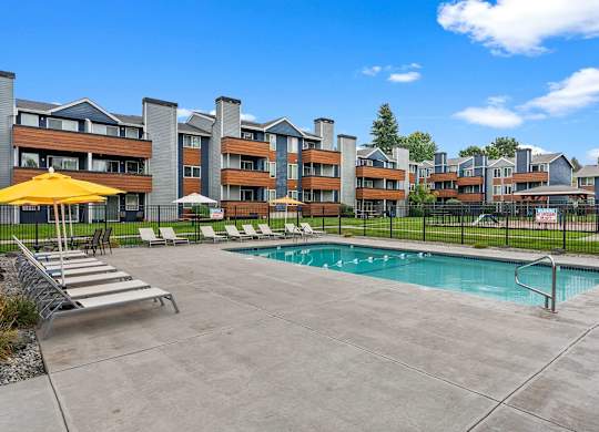 A pool area with a yellow umbrella and lounge chairs in front of a multi-story apartment building. at Northpoint Apartments, Tacoma, WA, 98407