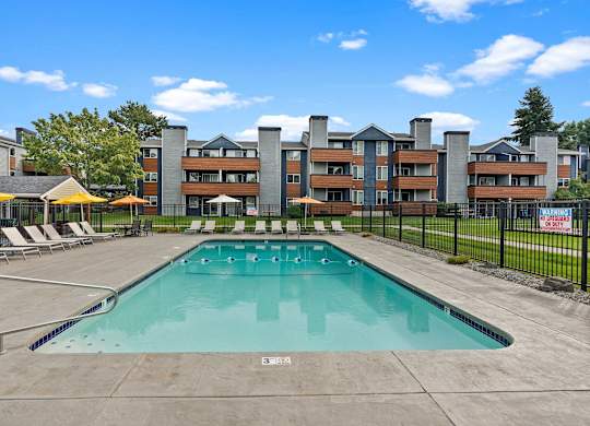 A large outdoor swimming pool with a concrete floor and a metal fence surrounding it. at Northpoint Apartments, Tacoma