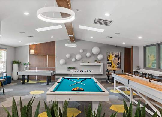 A pool table is in the middle of a room with a shelf and a painting on the wall. at Northpoint Apartments, Tacoma, WA
