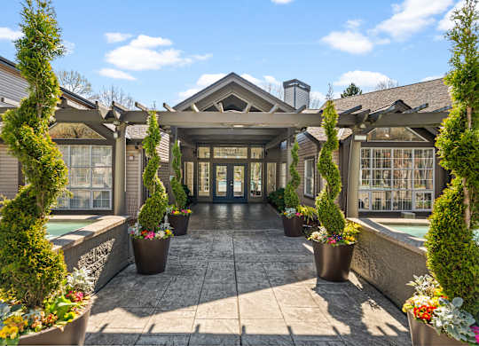 A building with a grey roof and a glass door is surrounded by green plants.